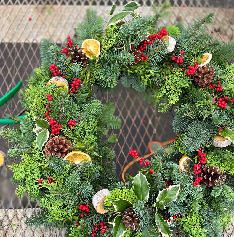 
                  
                    Berry evergreen wreath decorated with red berries, pinecones, dried orange slices and variegated leaves.
                  
                