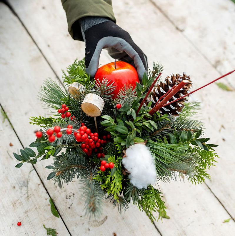 Overhead view of a holiday centerpiece with evergreens, red berries, pinecone and apple.